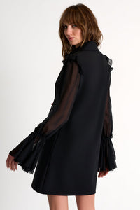 Woman wearing a black dress with sheer sleeves on a white background
