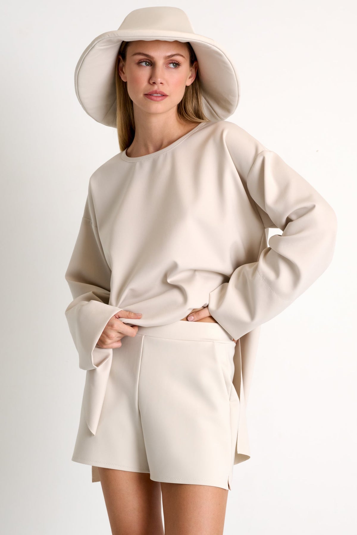 Woman wearing a beige outfit with a wide-brimmed hat on a white background