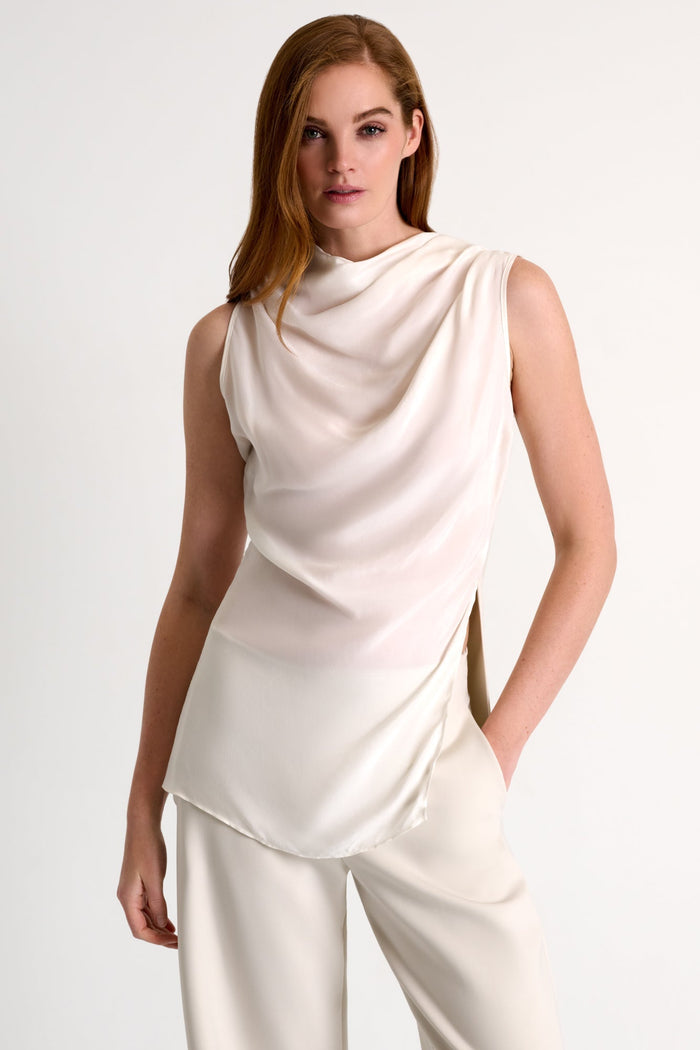 Woman wearing a light beige sleeveless top and pants on a plain background