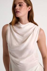 Woman wearing a beige sleeveless top against a white background