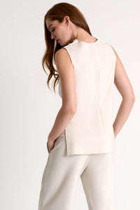 Woman wearing a sleeveless cream top and beige pants on a light gray background