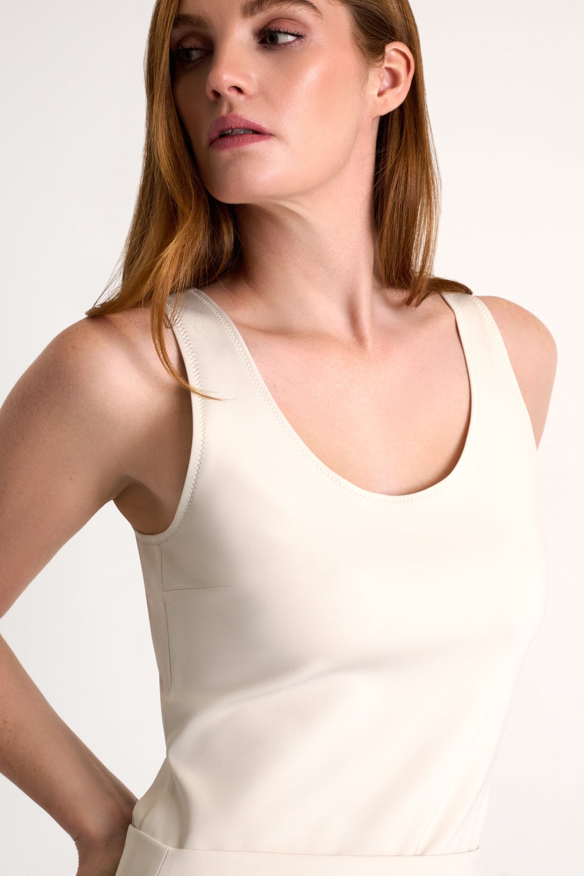 Woman wearing a beige sleeveless top against a plain background