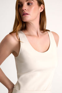 Woman wearing a beige sleeveless top against a plain background