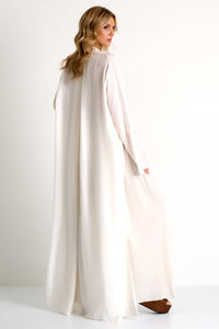 Woman wearing a long, light-colored dress with a cape on a white background