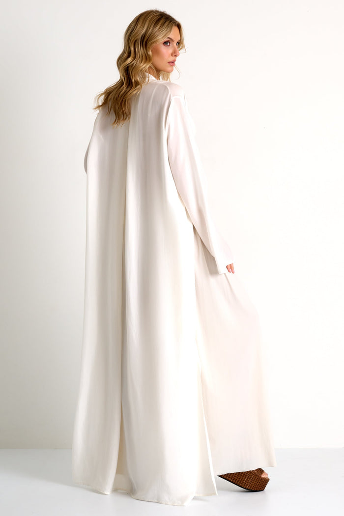 Woman wearing a long, light-colored dress with a cape on a white background