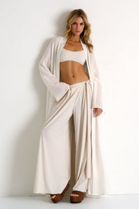 Woman wearing a white outfit with a flowing garment against a plain background
