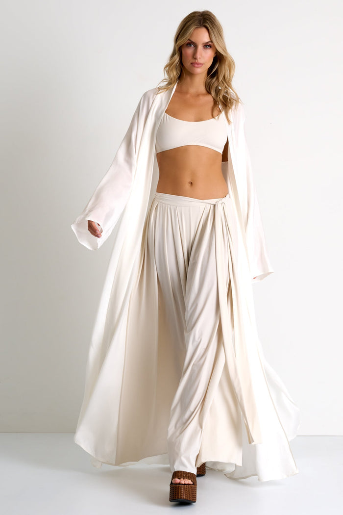 Woman wearing a white outfit with a long robe-like garment on a plain background