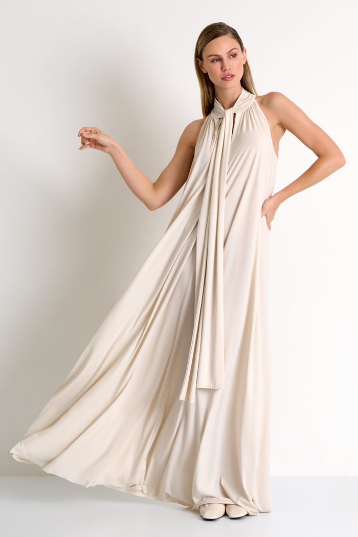 Woman wearing a flowing beige dress against a plain background