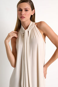 Woman wearing a beige halter neck dress against a white background