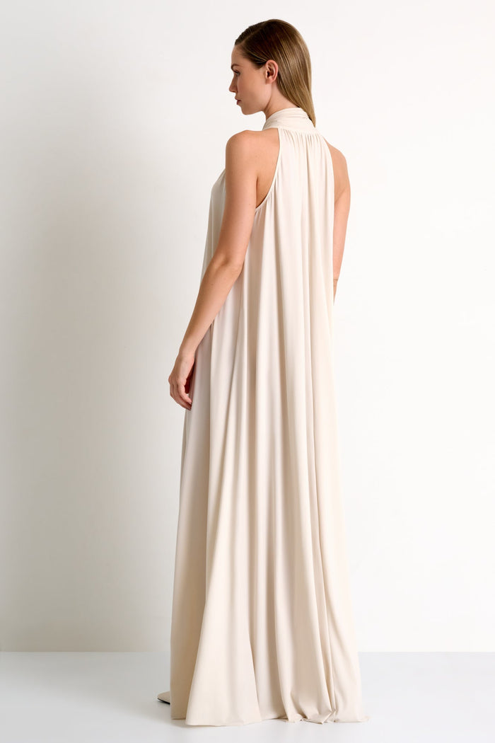 Woman wearing a long, flowing beige dress against a plain background