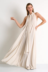 Woman wearing a flowing beige dress against a plain background