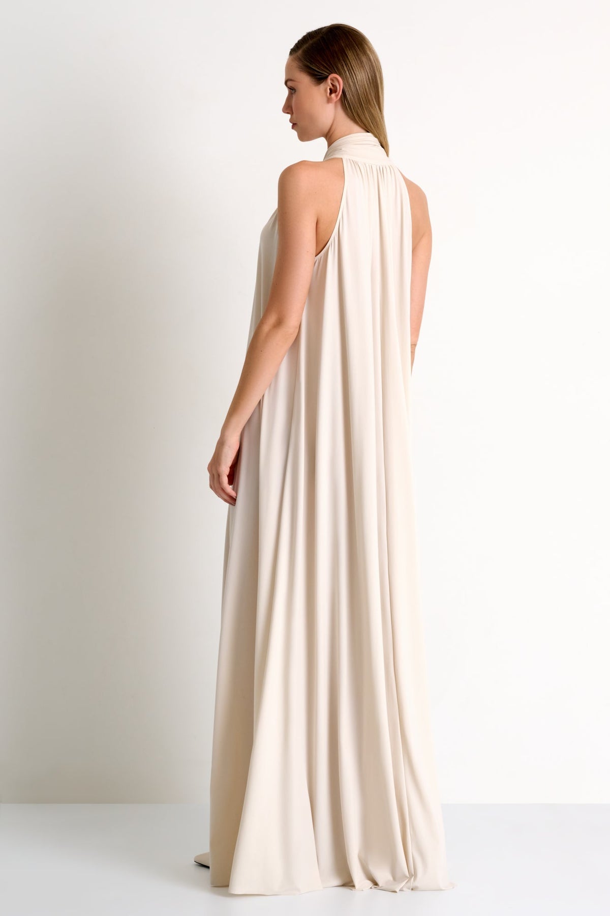 Woman wearing a long, flowing beige dress against a plain background