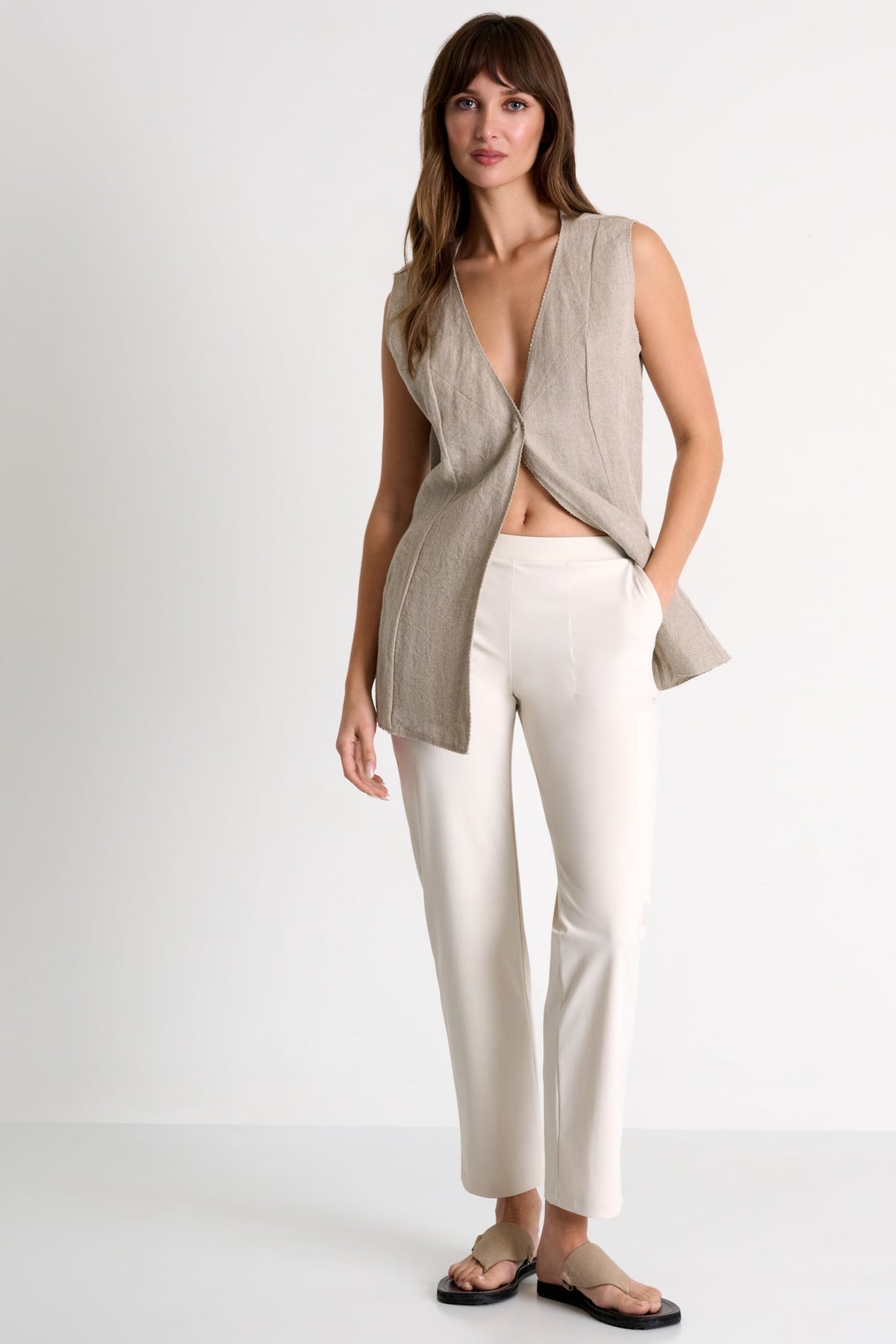 Woman wearing a beige sleeveless top and white pants on a white background