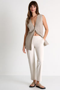 Woman wearing a beige sleeveless top and white pants on a white background