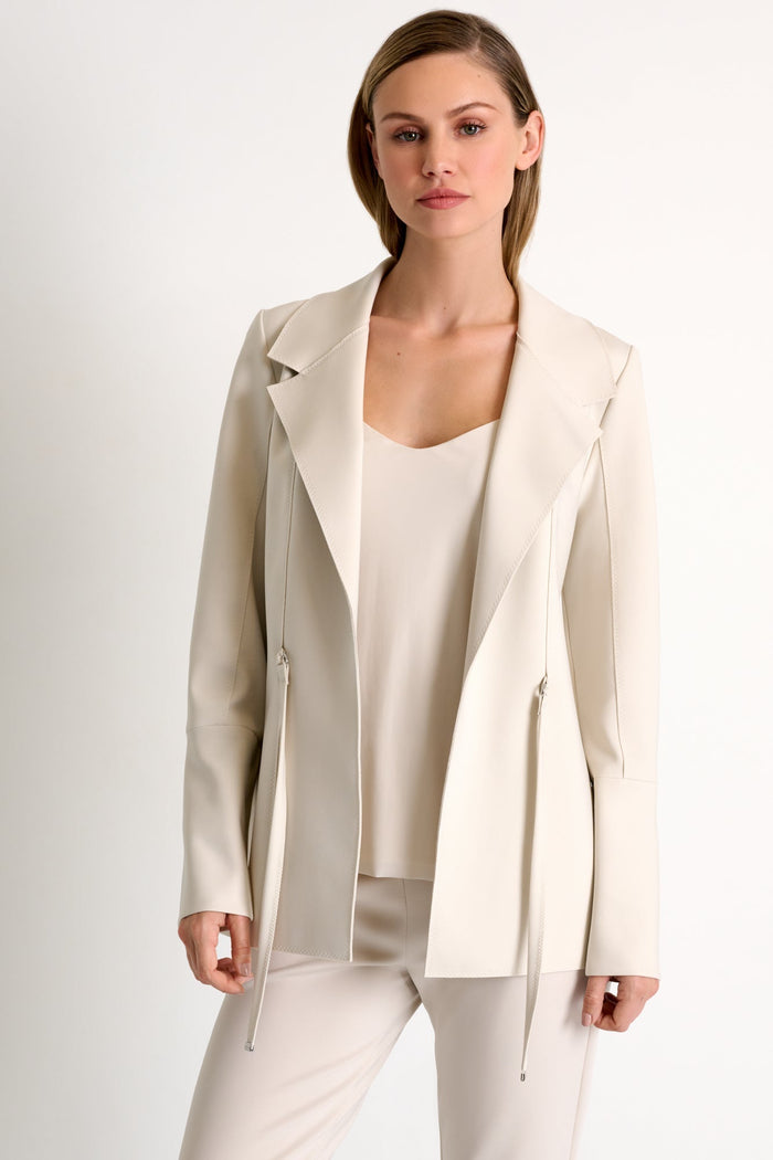 Woman wearing a beige blazer over a white top and pants on a plain background