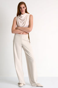 Woman wearing a sleeveless beige top and white pants on a white background