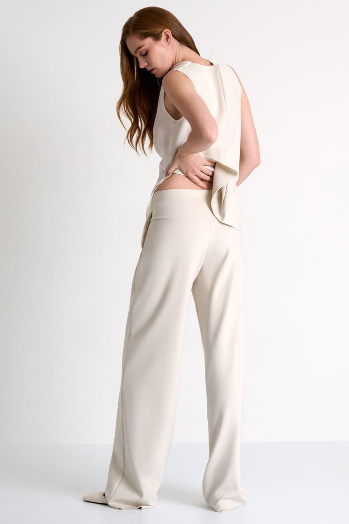 Woman wearing a beige sleeveless top and wide-leg pants on a white background