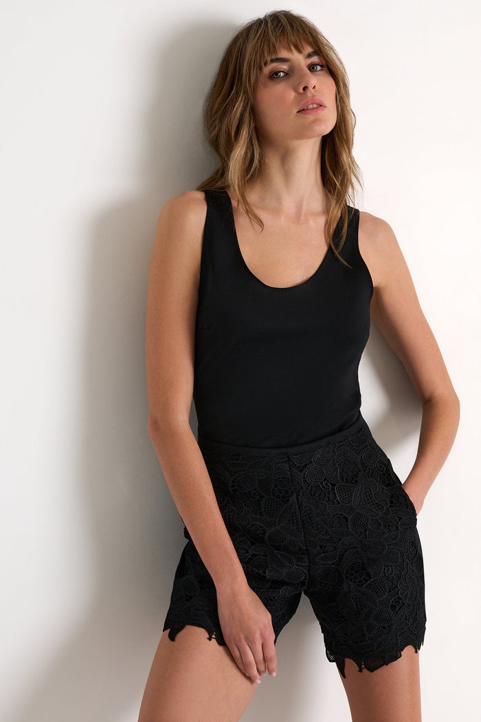 Woman wearing a black tank top and black shorts against a white background