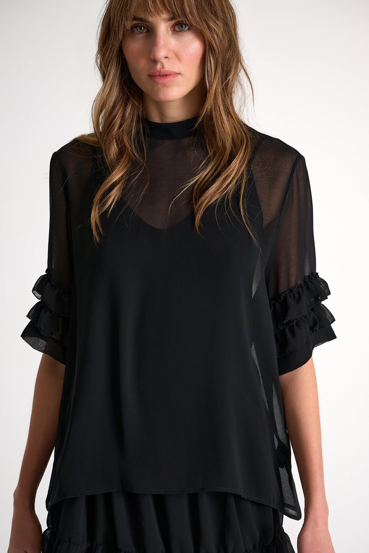Woman wearing a black layered outfit with sheer sleeves against a white background