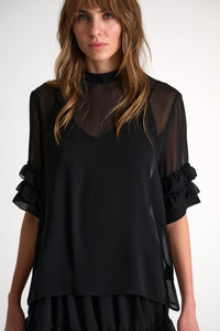 Woman wearing a black layered outfit with sheer sleeves against a white background
