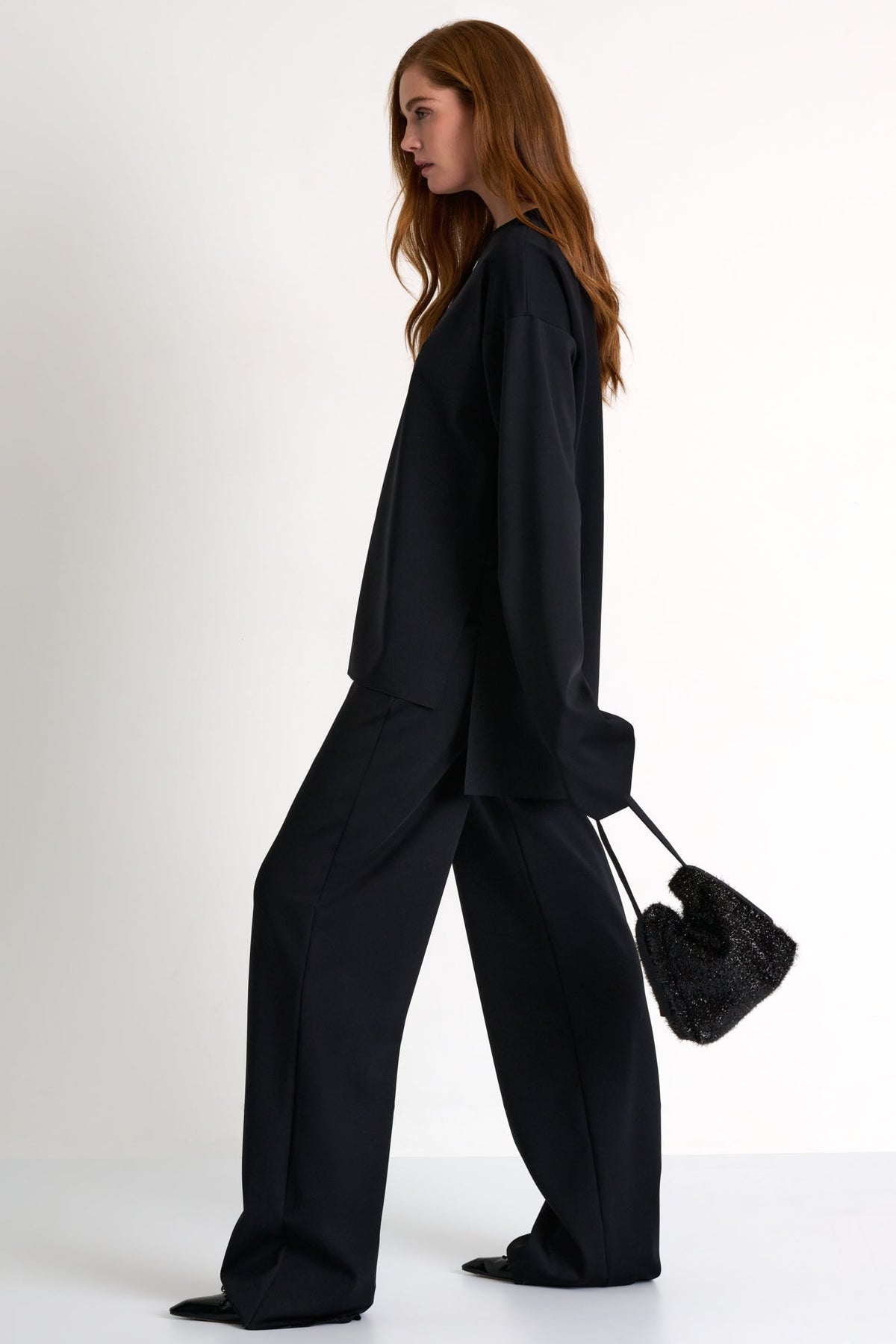 Woman wearing a black outfit holding a textured black bag on a white background