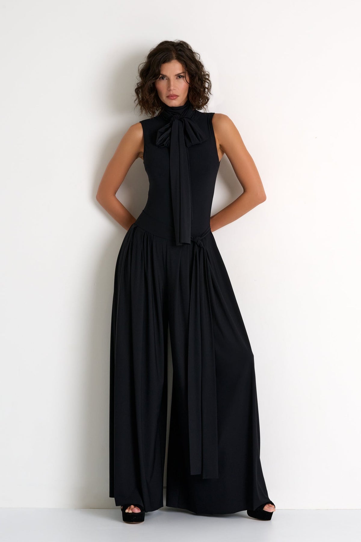 Woman wearing a black sleeveless dress with a large bow detail on a white background
