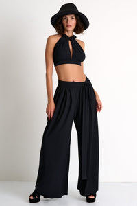 Woman wearing a black halter top and wide-leg pants with a black hat on a white background