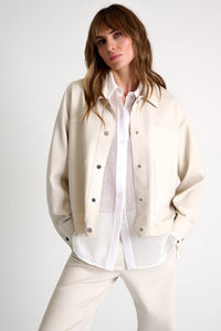 Woman wearing a beige jacket over a white shirt on a plain background