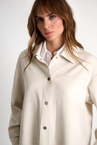 Woman wearing a beige coat over a white shirt on a plain background