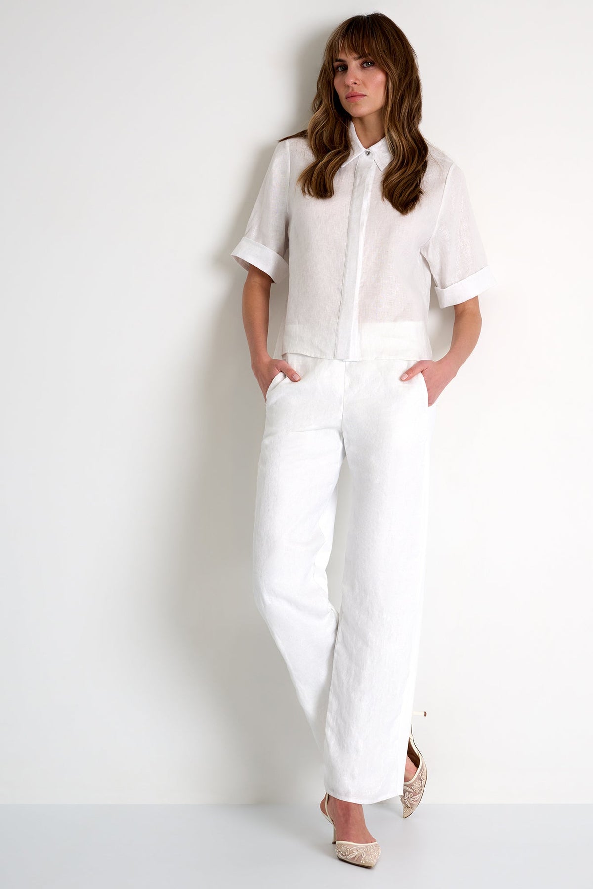 Woman wearing a white linen shirt and pants against a white background