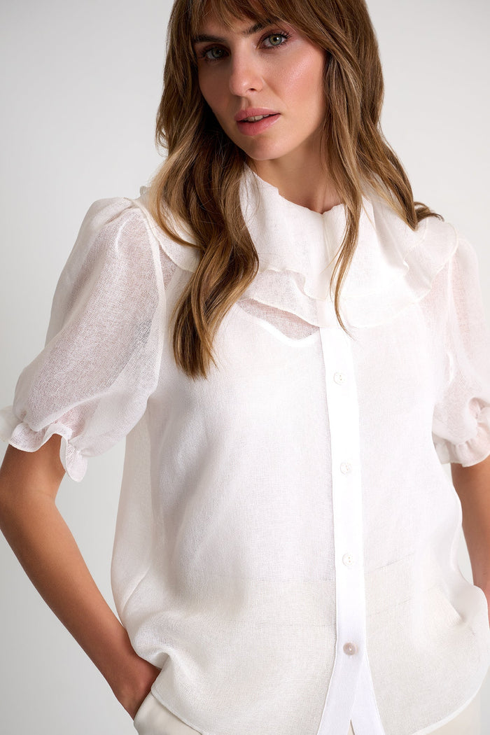 Woman wearing a white blouse with sheer sleeves against a plain background