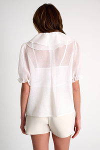 Person wearing a sheer white blouse and shorts on a plain background