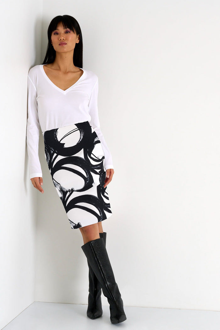 Woman wearing a white long-sleeve top and black and white patterned skirt with black knee-high boots against a white background.
