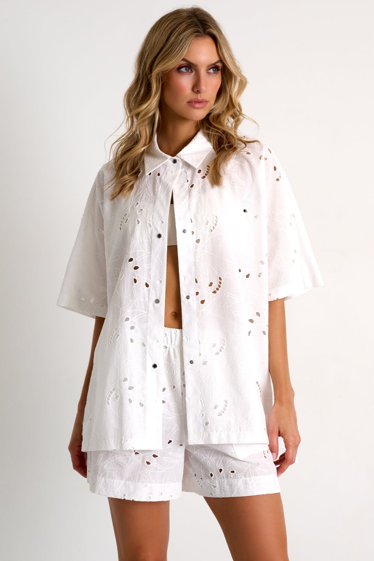 Woman wearing a white outfit with cut-out details on a plain background