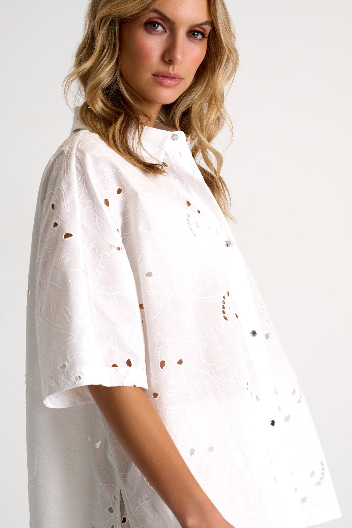 Woman wearing a white blouse with cut-out details on a plain background
