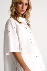 Woman wearing a white blouse with cut-out details on a plain background