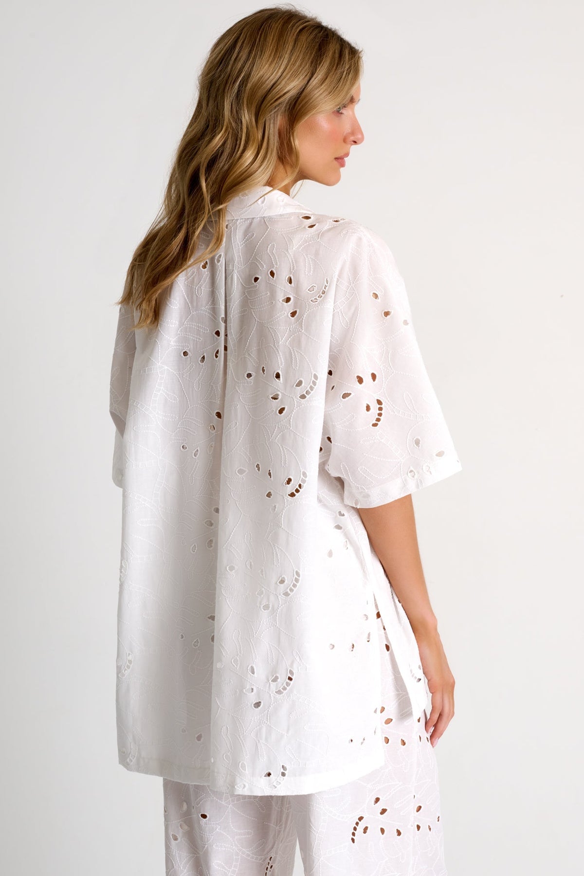 Woman wearing a white outfit with subtle patterns on a plain background