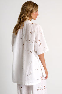 Woman wearing a white outfit with subtle patterns on a plain background